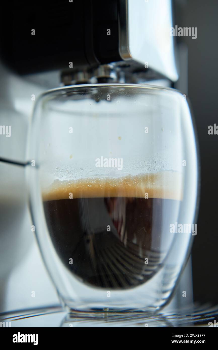 Frischer Espresso in klarem Glas am Morgen. Kaffeemaschine auf dunklem Hintergrund, Nahaufnahme. Moderne Kaffeemaschine mit frisch gebrühtem Kaffee in Glasbecher. Ki Stockfoto