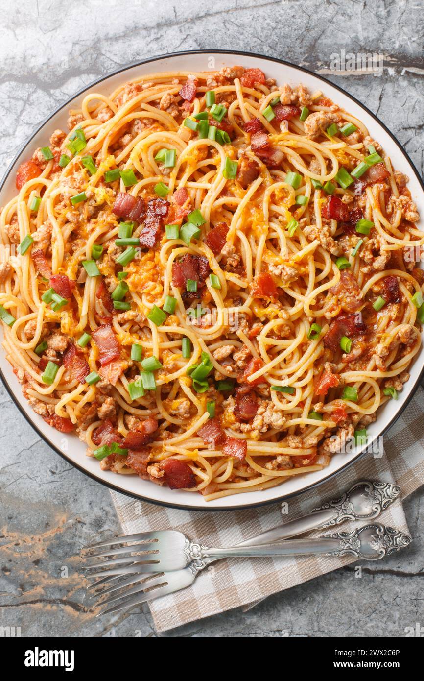 Cowboy-Spaghetti mit Hackfleisch, Speck, Cheddar-Käse, Zwiebeln, Pfeffer und Tomaten aus der Nähe auf dem Teller auf dem Tisch. Vertikale Draufsicht von oben Stockfoto