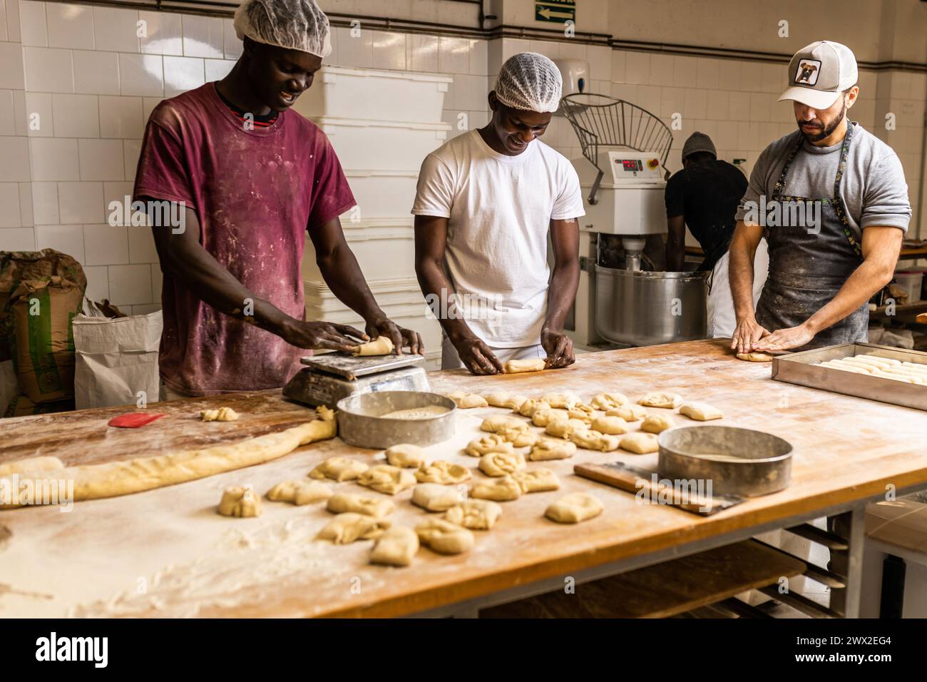 Zwei Männer, junge schwarze Klassenkameraden, die lernen, wie man Kuchen macht, vom Meister des Konditors in der Brotfabrik Stockfoto
