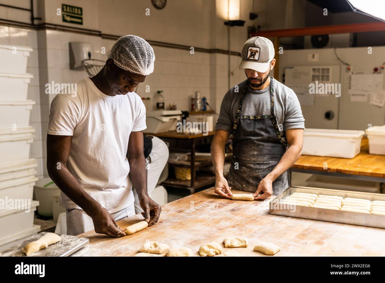 Junge schwarze Klassenkameraden lernen, wie man Kuchen macht, vom Meister der Konditorei in der Brotfabrik Stockfoto