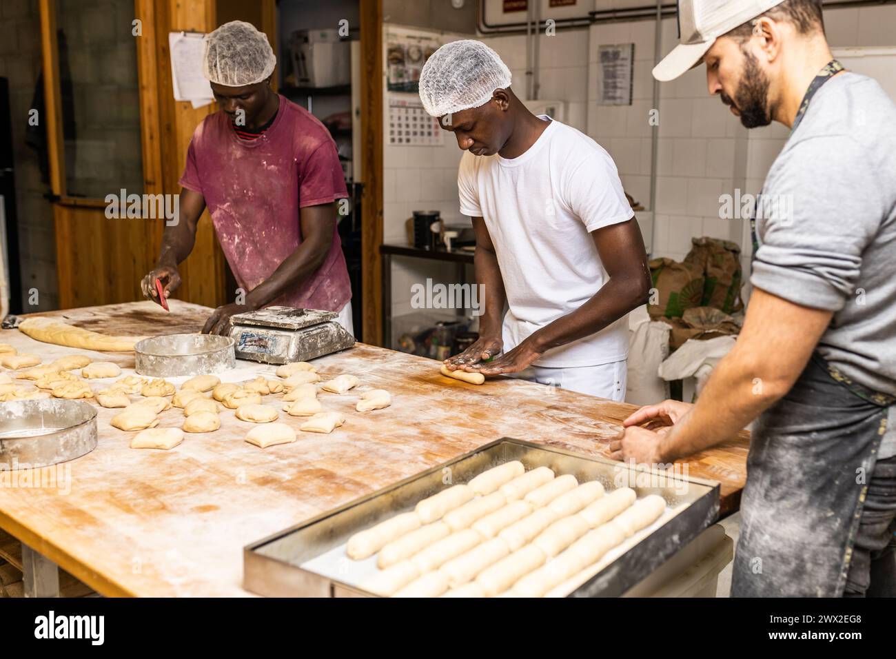 Zwei Männer, junge schwarze Klassenkameraden, die lernen, wie man Kuchen macht, vom Meister des Konditors in der Brotfabrik Stockfoto