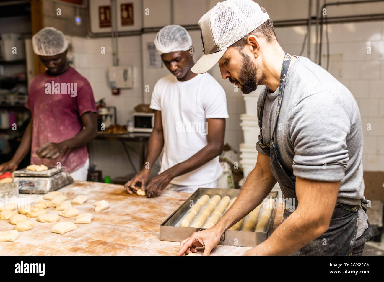 Zwei Männer, junge schwarze Klassenkameraden, die lernen, wie man Kuchen macht, vom Meister des Konditors in der Brotfabrik Stockfoto