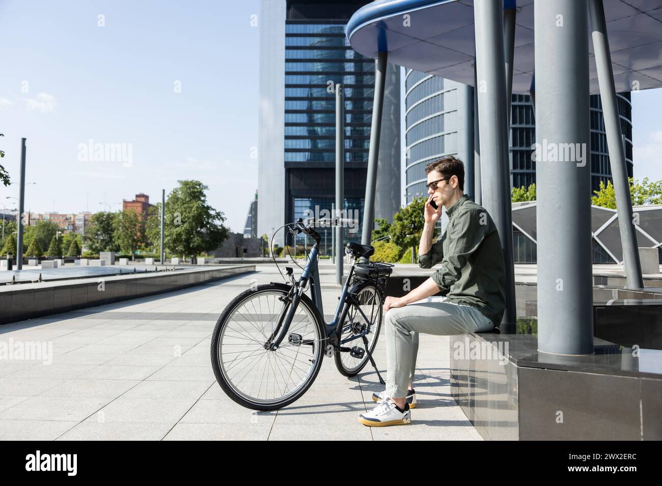 Ein junger Geschäftsmann fährt E-Bike auf dem Weg zum Turm, in dem sich sein Büro befindet Stockfoto