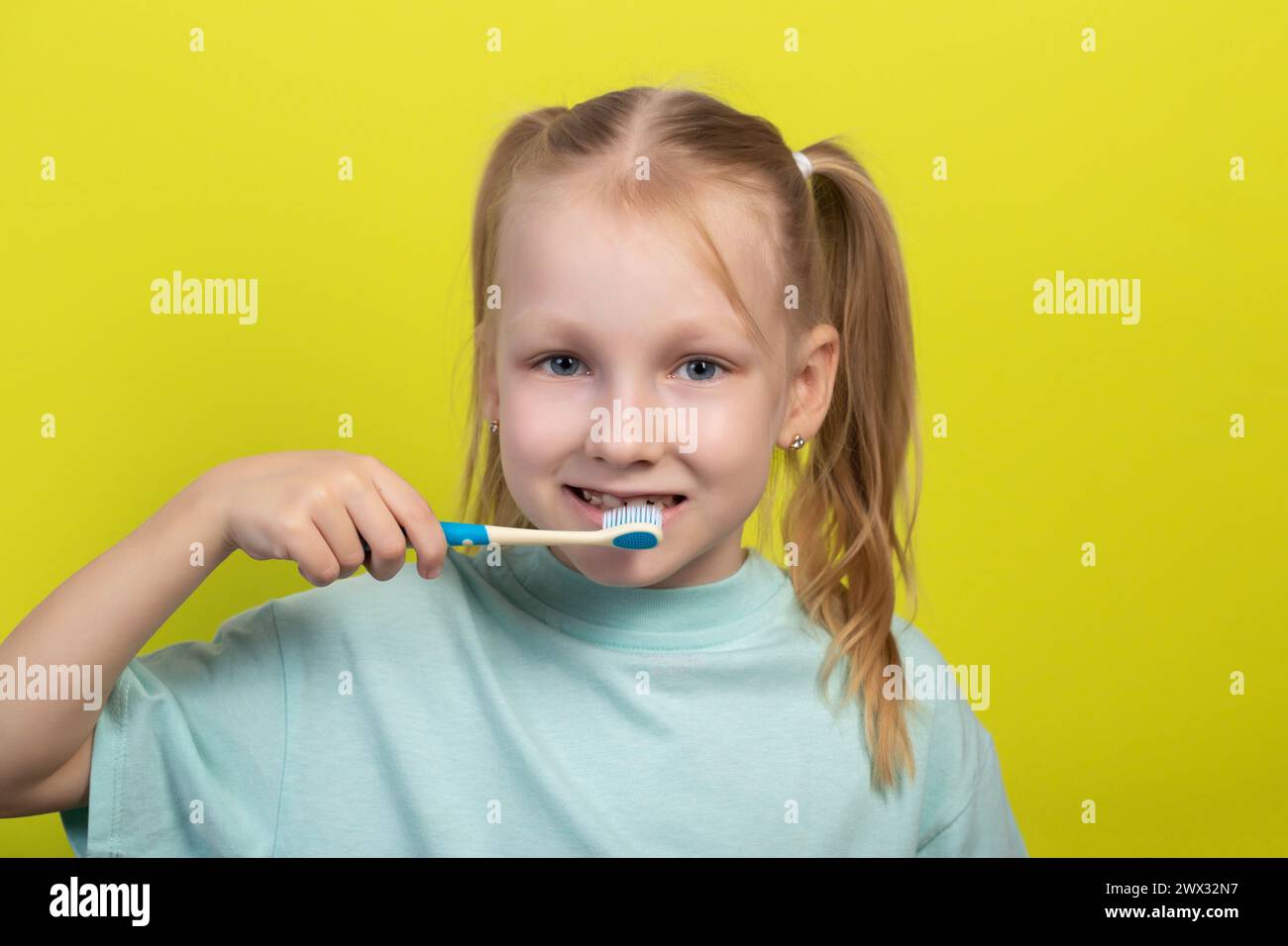 Das Gesicht eines lächelnden siebenjährigen Mädchens auf gelbem Hintergrund mit einer Zahnbürste in den Händen. Konzept der Zahnpflege und -Reinigung. Mundhygiene in d Stockfoto