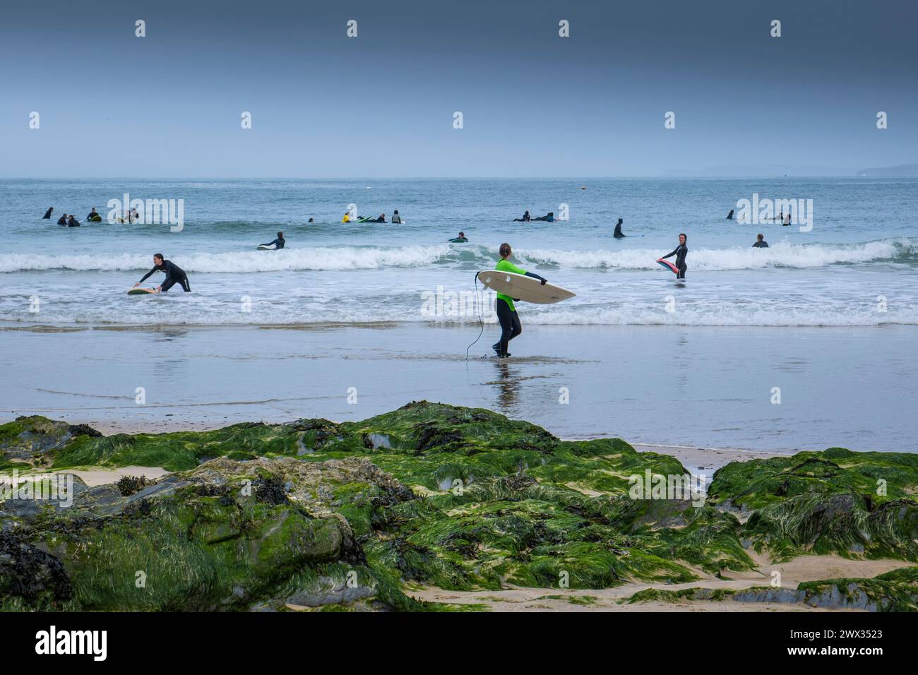 Eine Surferin, die nach dem Surfen am Towan Beach in Newquay in Cornwall in Großbritannien mit ihrem Surfbrett aus dem Meer ging. Stockfoto