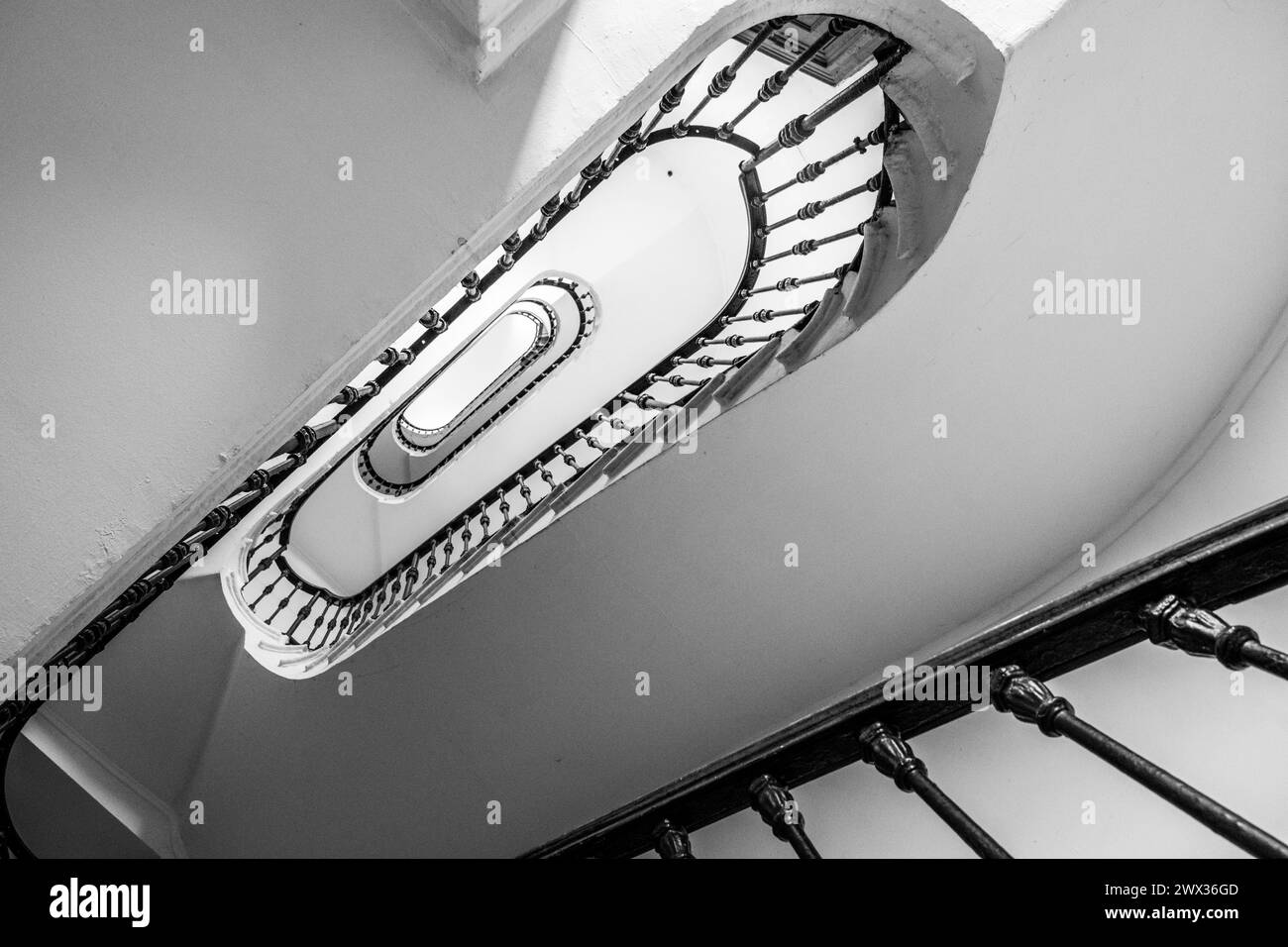 Ein fesselndes Schwarzweiß-Bild, das das komplizierte Design einer Wendeltreppe erfasst und die längliche ovale Form und das detaillierte Geländer betont. Die Perspektive bietet einen faszinierenden Blick, der den Blick nach oben zieht und architektonische Schönheit und Designpräzision zeigt. Schwarzweißbild. Stockfoto