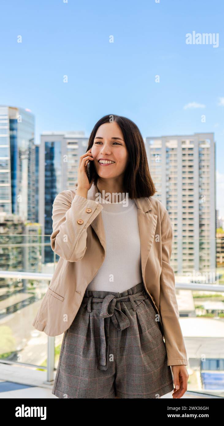 Eine lächelnde Unternehmerin benutzt ihr Smartphone, um sich mit jemandem zu unterhalten. Stockfoto