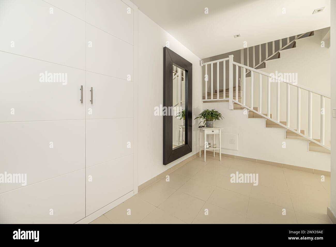 Flur eines mehrstöckigen Einfamilienhauses mit Einbauschränken, Treppen mit Metallgeländern und cremefarbenen Steinzeugböden Stockfoto