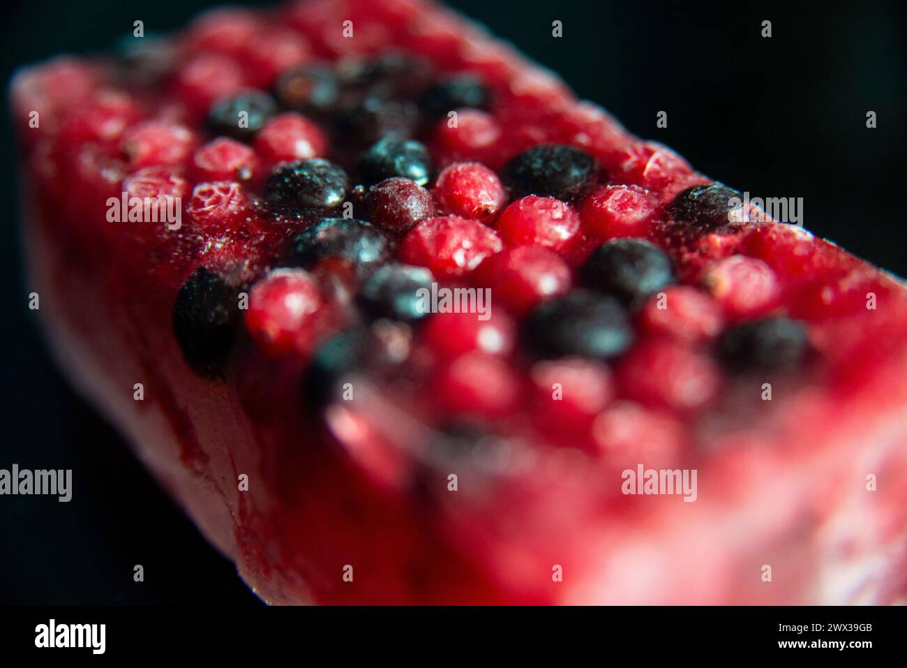 Gemischte rote und schwarze Beeren, gefroren in einem Eisblock vor schwarzem Hintergrund. Gefrorene Frucht- oder Smoothie-Mischung. Stockfoto