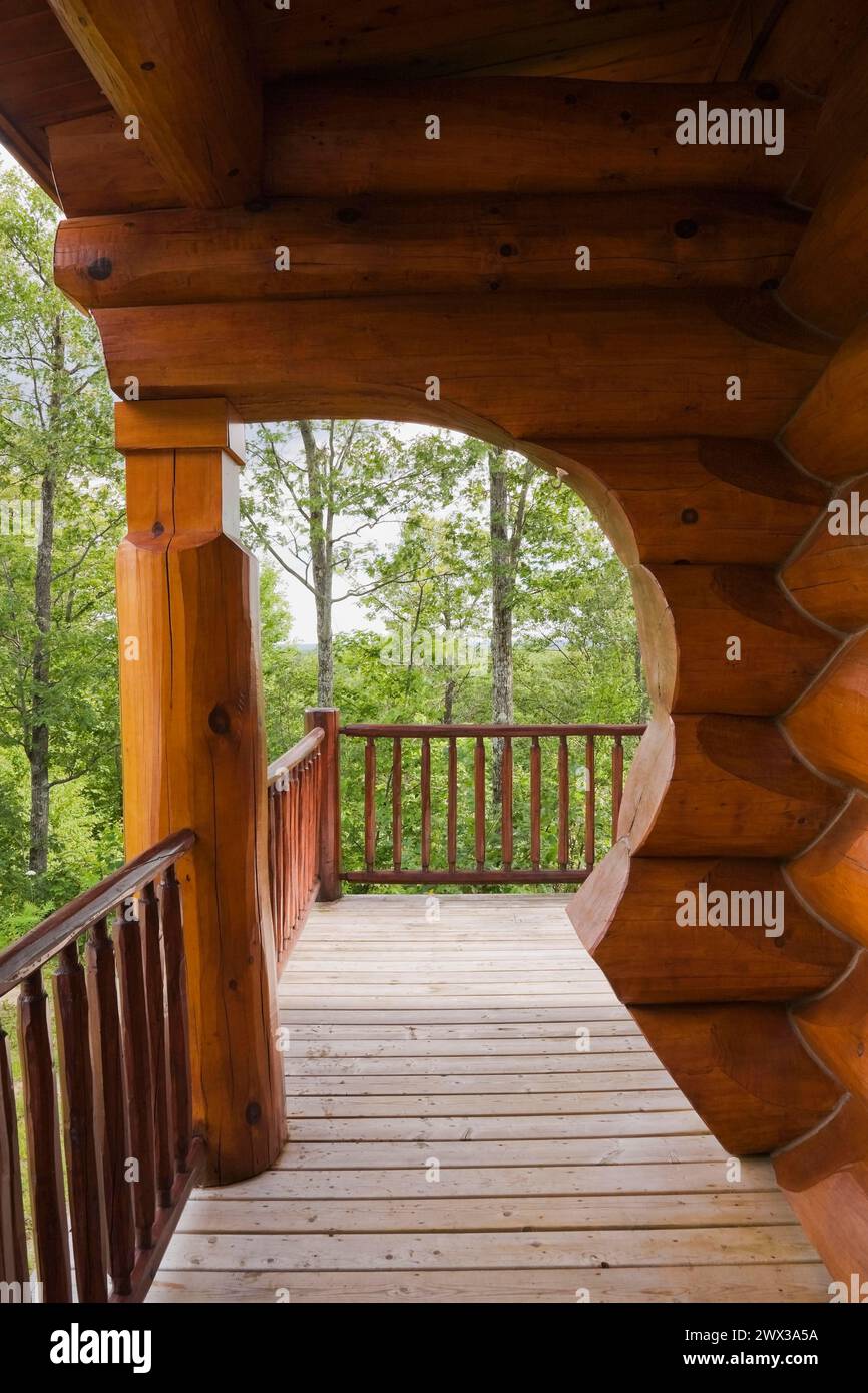 Braunes rötlich gebeiztes skandinavisches Blockhaus mit Bogen und Wand aus großen gezackten Stämmen und Holzdielen Veranda im Sommer, Quebec, Kanada Stockfoto