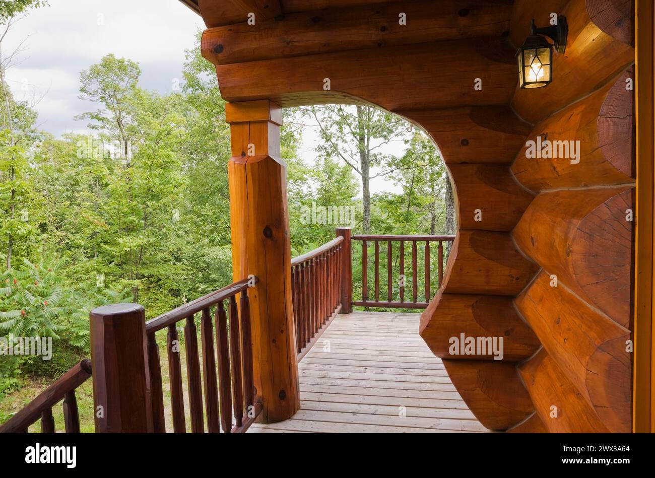 Braunes rötlich gebeiztes skandinavisches Blockhaus mit Bogen und Wand aus großen gezackten Stämmen und grauer Holzdiele Veranda im Sommer, Quebec Stockfoto