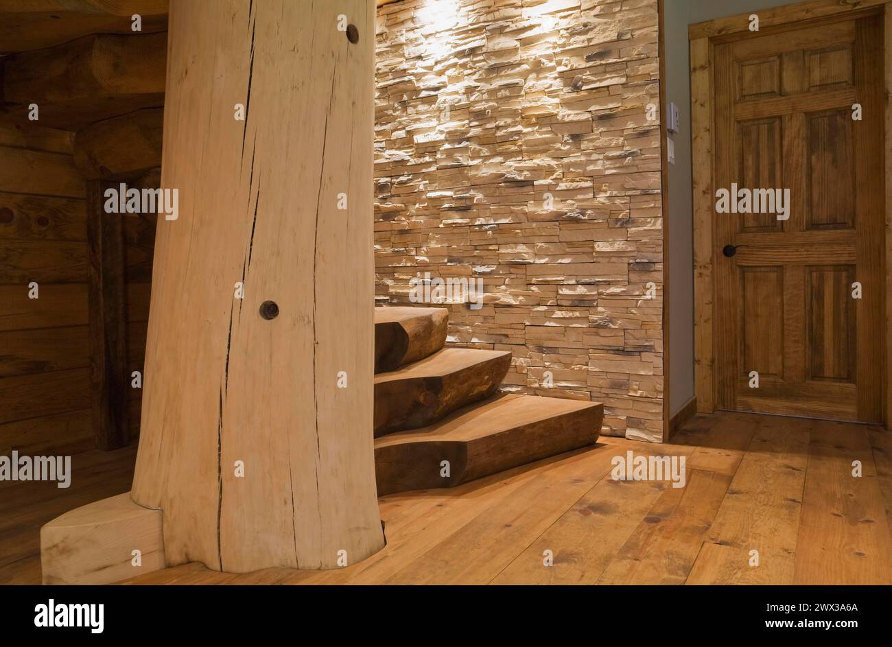 Tür und verwinkelte Holztreppe mit braun gebeizten Stufen aus Halbholz, die an einem großen gebleichten Stützpfosten befestigt und beleuchtet sind Stockfoto