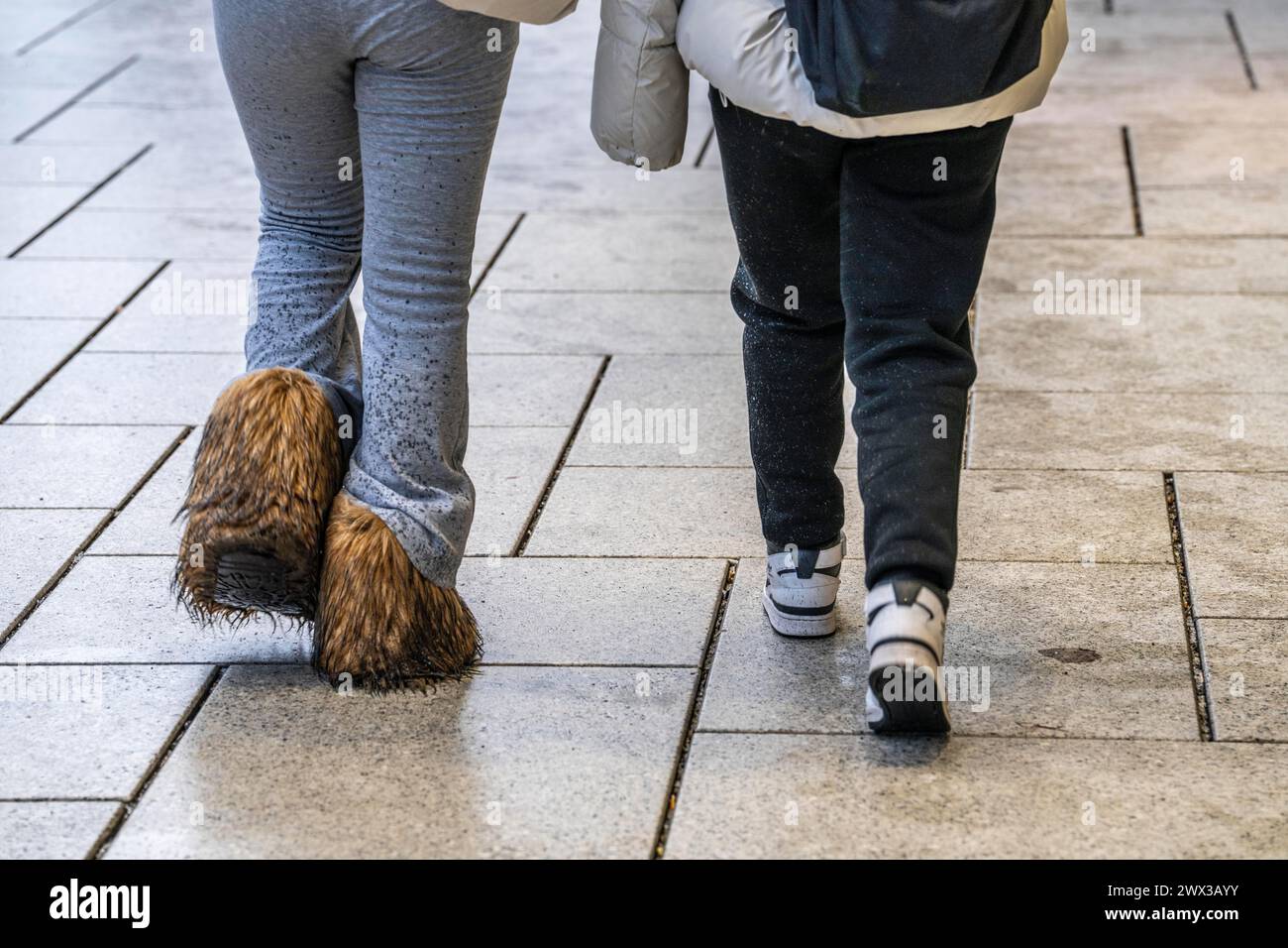 2 Frauen, die im Regen laufen, eine Frau trägt Stiefel mit langem Fell, nass, schmutzig, Wasserspritzer auf der Hose, Stockfoto