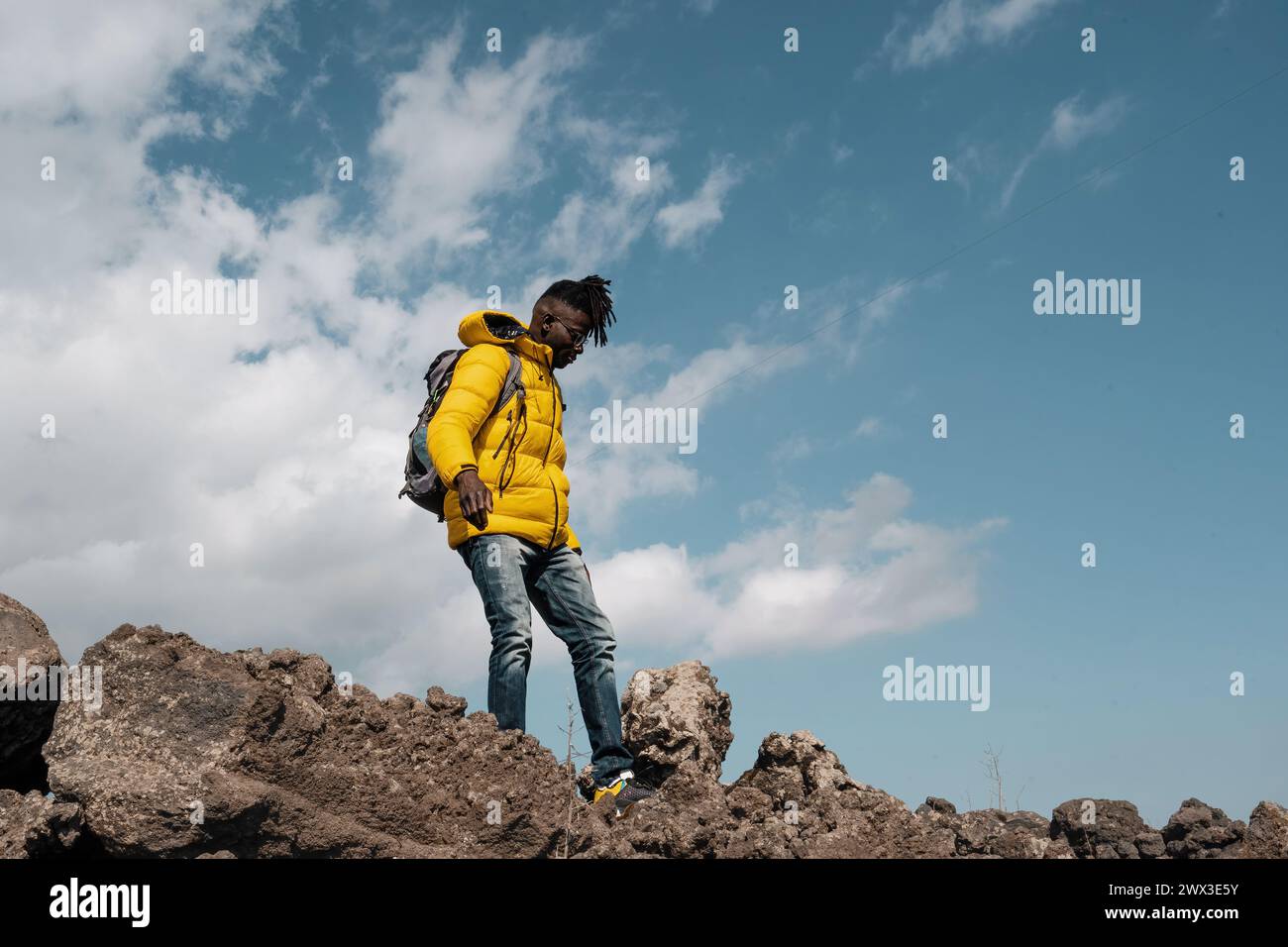 Junger Mann mit leuchtender gelber Jacke - Wandern felsige Landschaft, Abenteuermode - klarer Himmel, Outdoor-Erkundung - Kopierraum. Stockfoto