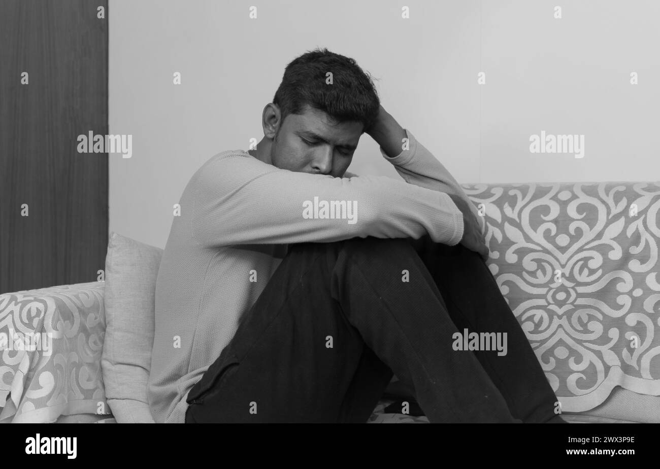 Schwarz-weiß Ein junger Indianer sitzt auf einem Sofa, nachdenklich und tief in Gedanken. Sein Ausdruck traurig Stockfoto