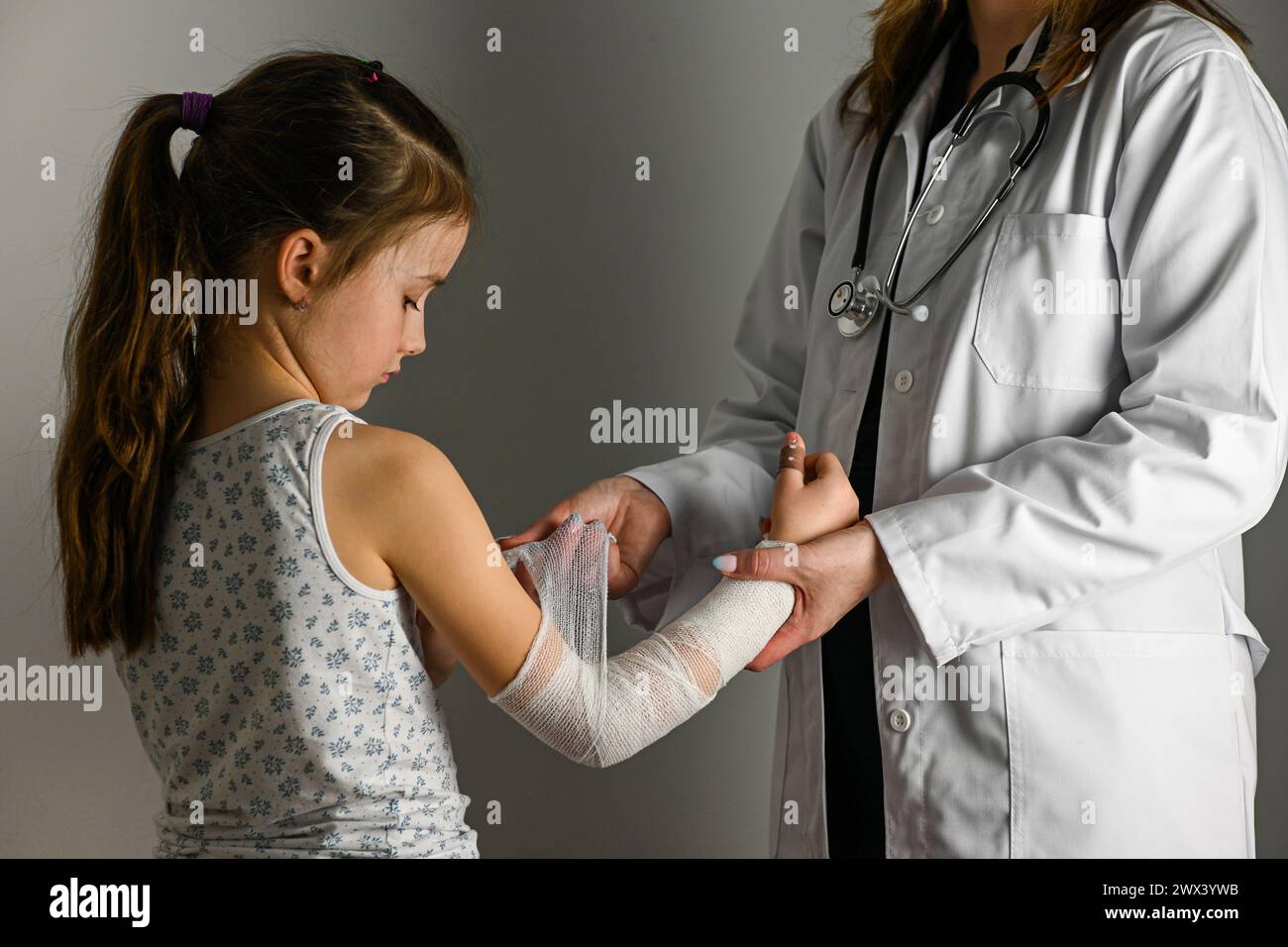 Ein Arzt in einem weißen Mantel mit einem Stethoskop verbindet die Hand eines kleinen Mädchens. Stockfoto