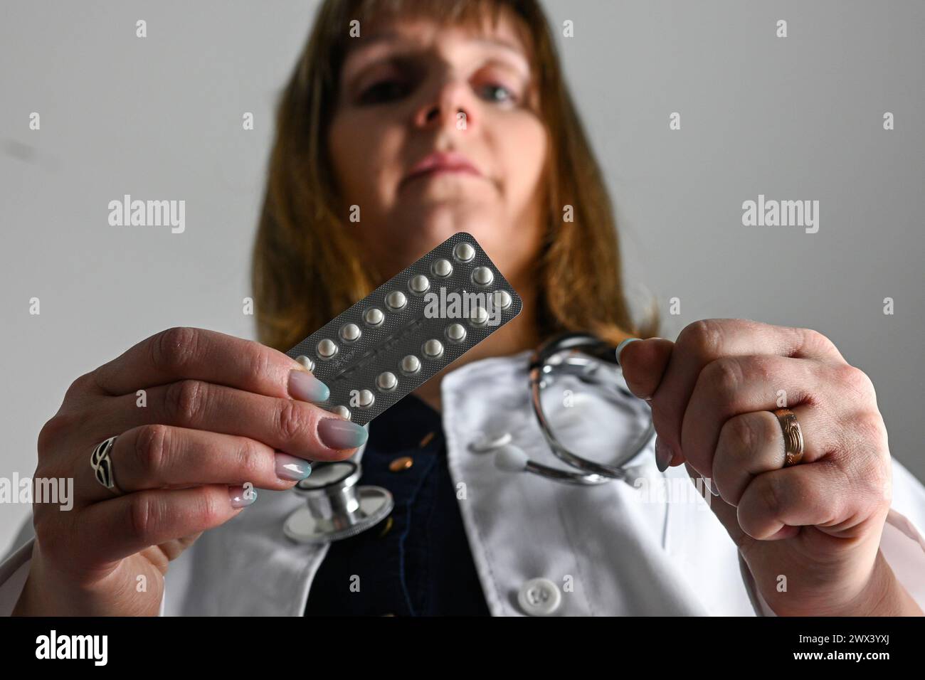 Ein Arzt in einem weißen Mantel mit einem Stethoskop hält Verhütungspillen in der Hand, verschwommener Hintergrund. Stockfoto