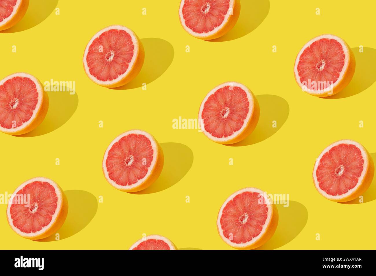 Trendiges Sonnenlicht-Fruchtmuster mit roter Grapefruitscheibe auf gelbem Hintergrund. Minimales Sommerkonzept. Kreative Essensidee. Grapefruitästhetik. Stockfoto