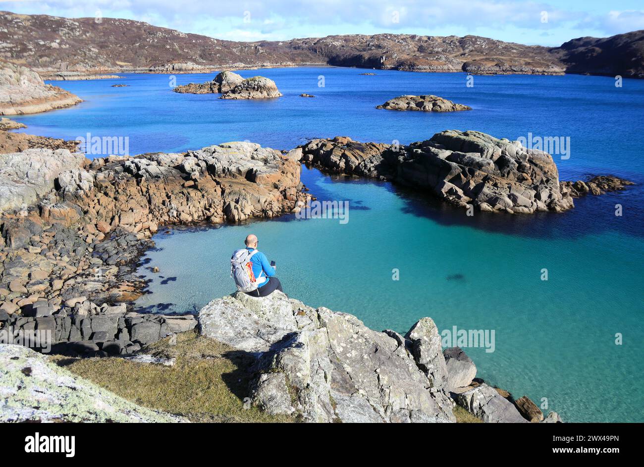 Isle of Mull, Mann auf Felsen mit Blick auf das wunderschöne klare Meer von Port na Ron, einer abgelegenen Bucht am Ross of Mull, Schottland Stockfoto