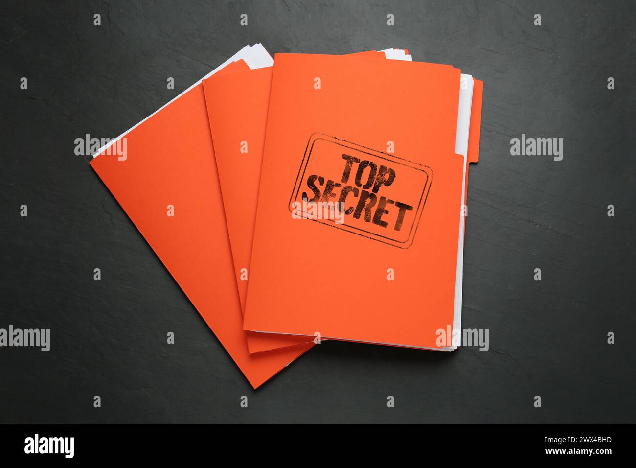 Streng geheimer Stempel. Orangefarbene Dateien mit Dokumenten auf schwarzer Tabelle, Draufsicht Stockfoto