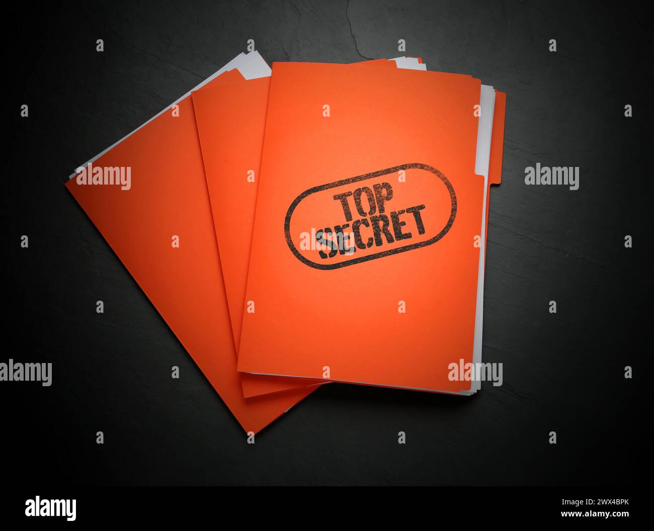 Streng geheimer Stempel. Orangefarbene Dateien mit Dokumenten auf schwarzer Tabelle, Draufsicht Stockfoto