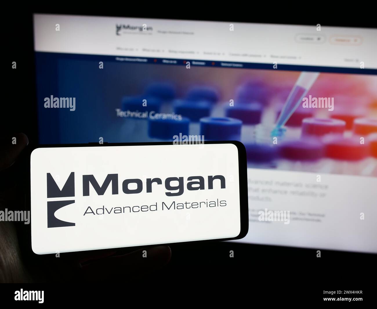 Person, die ein Mobiltelefon mit dem Logo des britischen Unternehmens Morgan Advanced Materials plc vor der Business-Webseite hält. Schwerpunkt auf dem Display des Telefons. Stockfoto