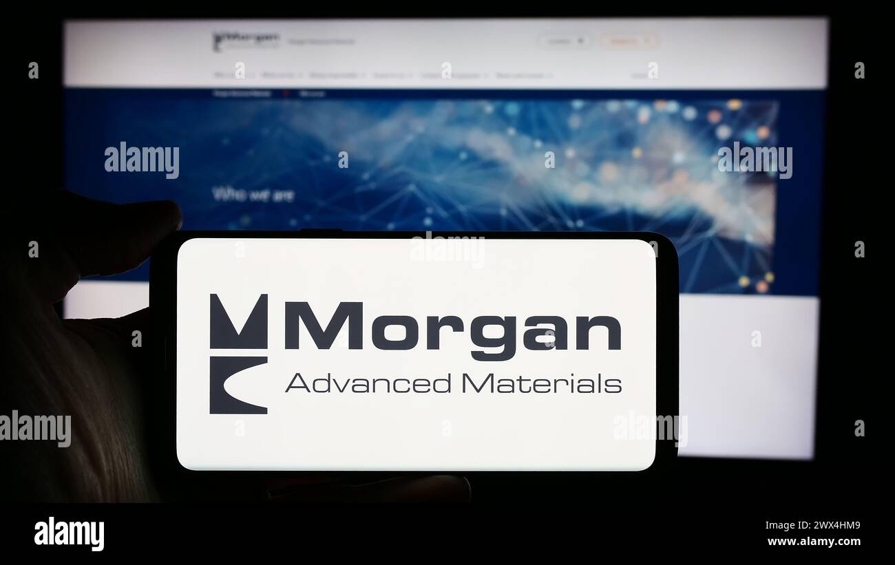 Person, die ein Mobiltelefon mit dem Logo des britischen Unternehmens Morgan Advanced Materials plc vor der Unternehmenswebseite hält. Schwerpunkt auf dem Display des Telefons. Stockfoto