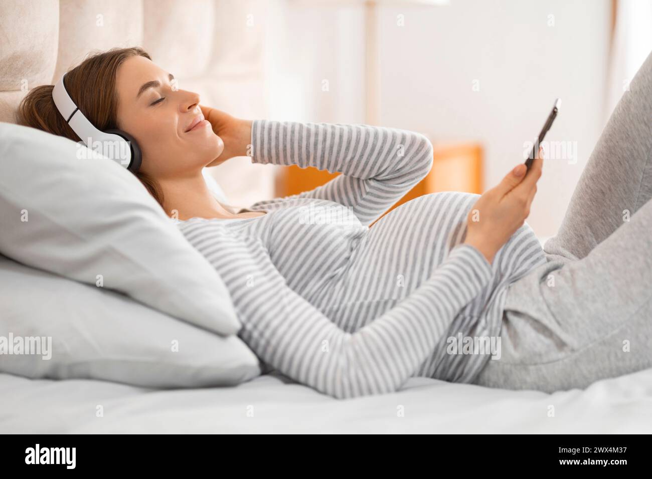 Frau, die mit Smartphone und Kopfhörern auf dem Bett liegt Stockfoto