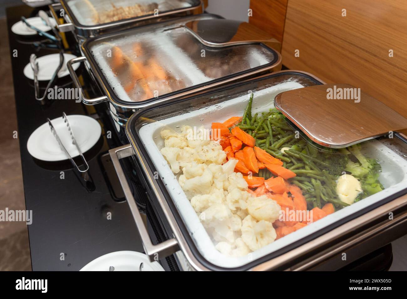 Frittiertes Fleisch auf Spießen und andere Vorspeisen in einem Essenswärmer auf einem Buffettisch in einem Hotelrestaurant. Tisch mit Geschirr und glänzenden Marmiten warten darauf Stockfoto