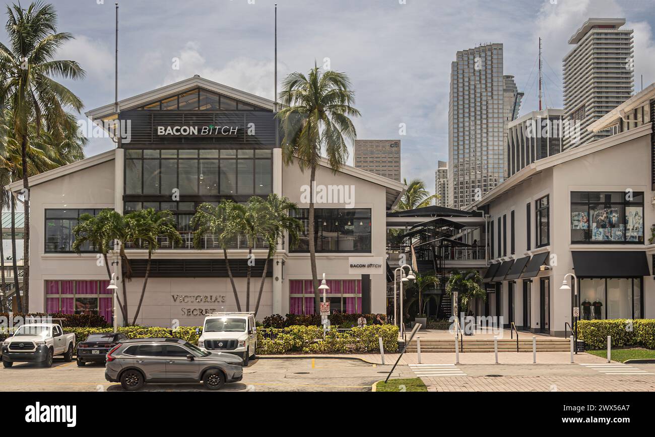 Miami, Florida, USA - 29. Juli 2023: Bacon Bitch Restaurant über Victoria Secret Dessous-Fassade am Port blvd. Grüne Pflanzen und Bäume. Autos Stockfoto