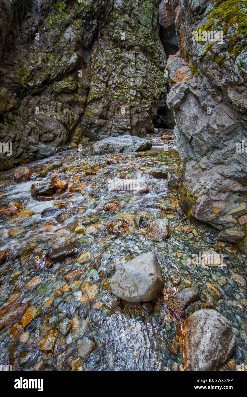 Ein klarer Bach fließt schnell durch eine zerklüftete Landschaft, umgeben von steilen, felsigen Klippen und Felsbrocken Stockfoto