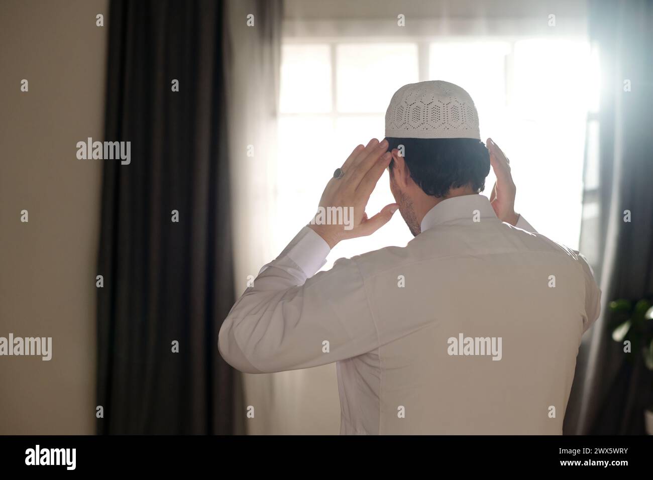 Rückansicht eines nicht erkennbaren jungen muslimischen Mannes, der weiße Thobe und Taqiyah trägt und salah betet, Kopierraum Stockfoto
