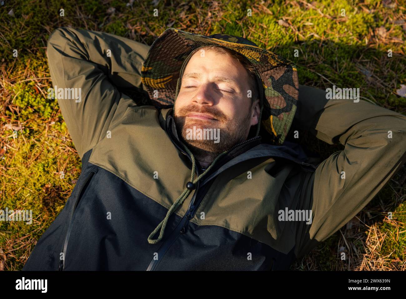 Friedlicher, zufriedener Mann, der auf grünem Waldmoos schläft und ausruht. Natur und Ruhe. Stressabbau und psychische Gesundheit Stockfoto
