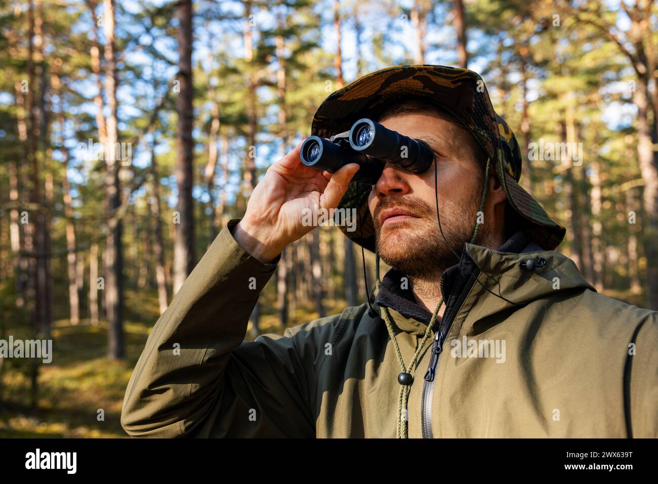 Mann in Tarnkleidung, der durch ein Fernglas im Wald schaut. parküberwachung, Vogelbeobachtung Stockfoto