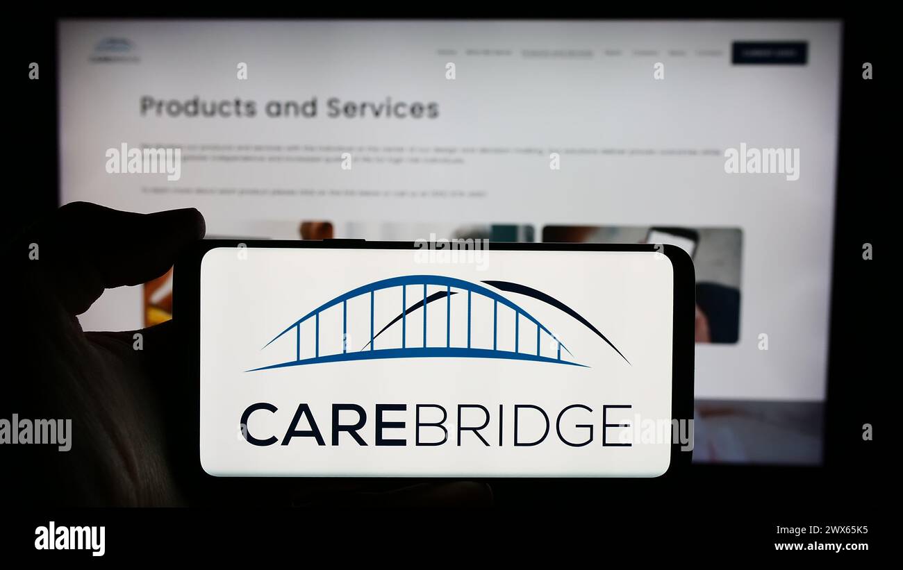 Person, die ein Mobiltelefon mit dem Logo des US-Gesundheitsunternehmens CareBridge vor der Business-Webseite hält. Schwerpunkt auf dem Display des Telefons. Stockfoto