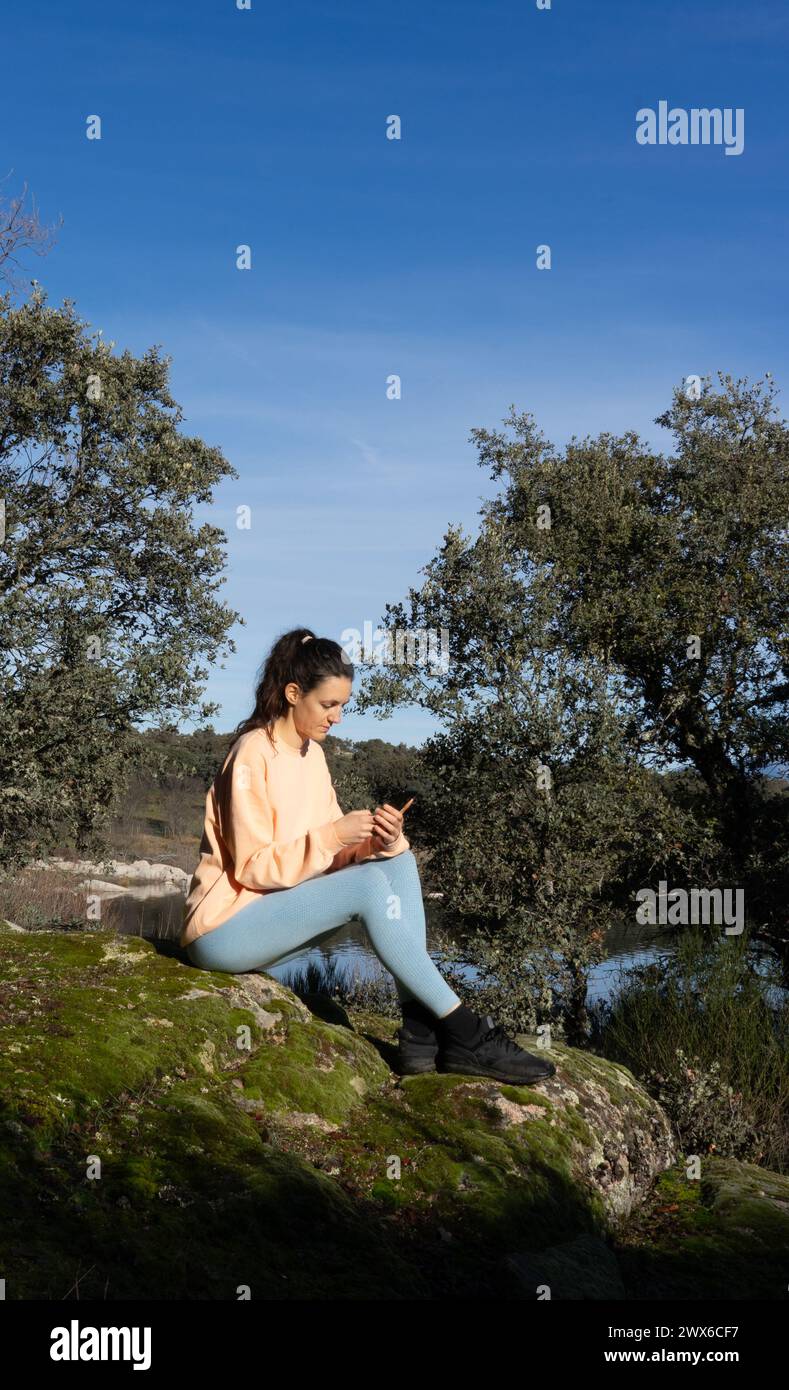 Frau, die in der Natur auf das Handy blickt, in pfirsichfarbener Farbe gekleidet Stockfoto