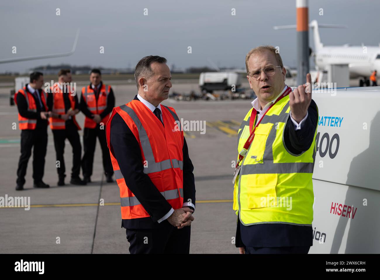 27. März 2024, Brandenburg, Schönefeld: Volker Wissing (FDP), Bundesminister für digitale Angelegenheiten und Verkehr, und Roland Ückert (r), Geschäftsführer der HiSERV GmbH, stehen vor einem elektrischen Erdkraftwerk (eGPU). Der Bundesverkehrsminister besuchte die HiSERV, um sich über eine nachhaltige Stromversorgung auf dem Vorfeld des Berliner BER-Flughafens zu informieren. Foto: Hannes P Albert/dpa Stockfoto