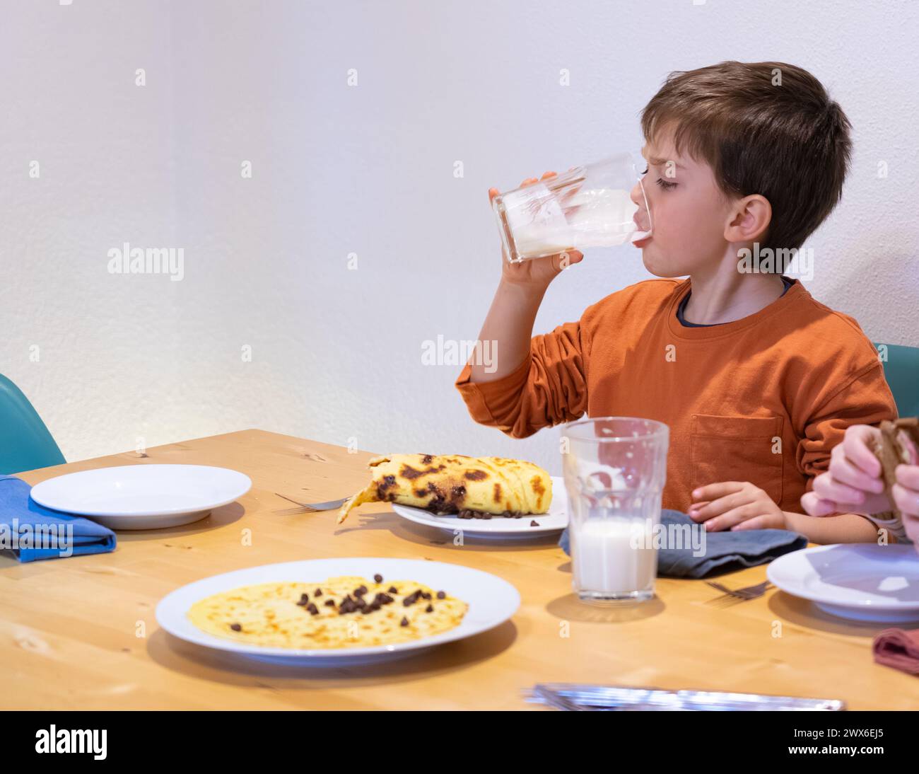Junge beim Frühstück, trinkt ein Glas Milch und isst einen Pfannkuchen Stockfoto