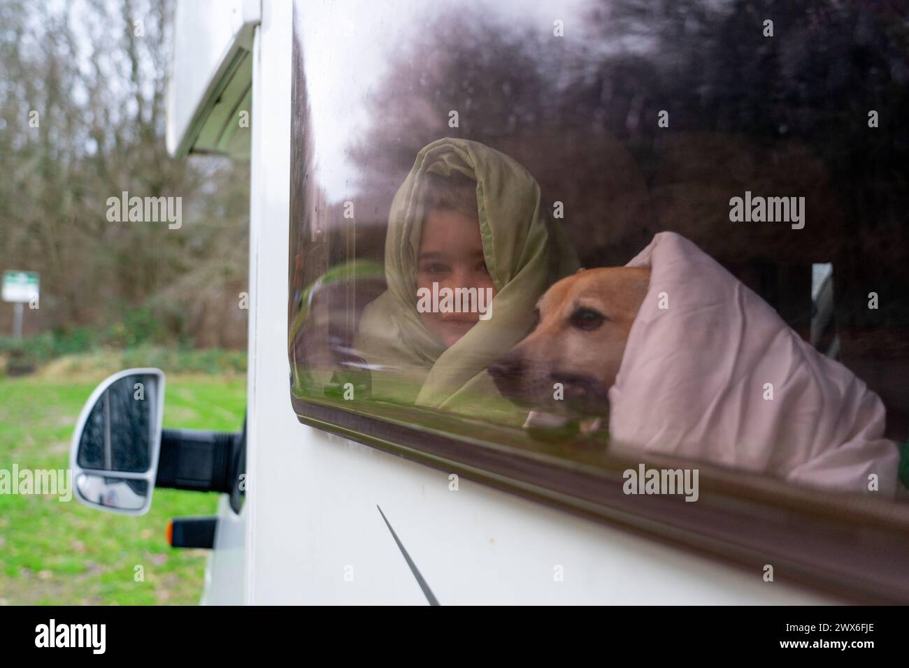 Junge mit seinem Hund, eingewickelt in Bettdecken und aus dem Fenster eines Wohnmobils schauen Stockfoto