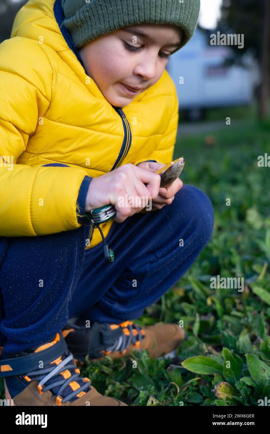 Junge, der einen Waldstock mit einem Taschenmesser schält, um einen Speer zu machen Stockfoto
