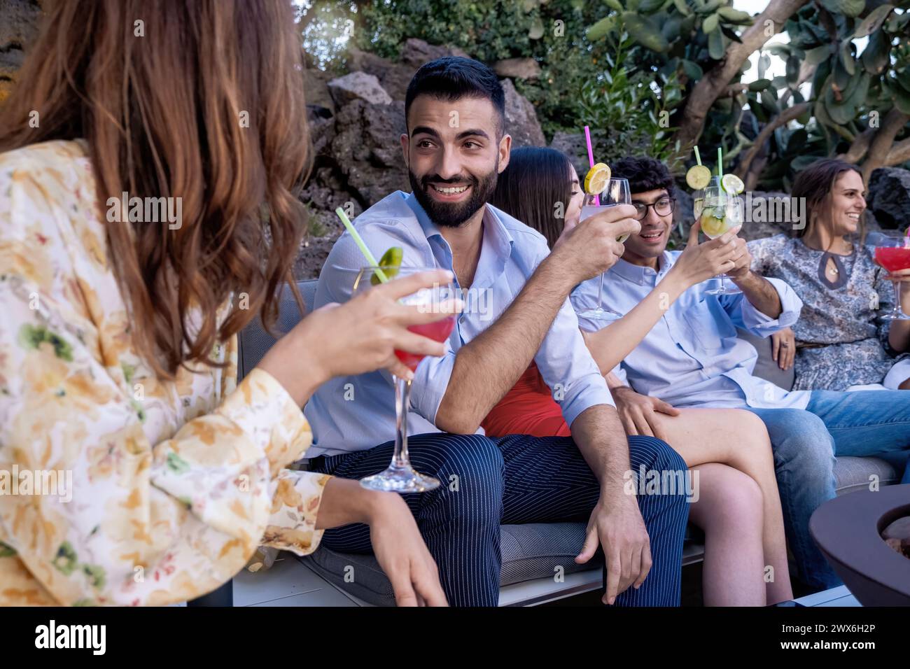 Lächelnder Mann beim Toasten - legere Gartenparty, stilvolle Gruppe mit Getränken - warmes Ambiente, gemeinsames Vergnügen - entspannende Sommertage mit Freunden. Stockfoto