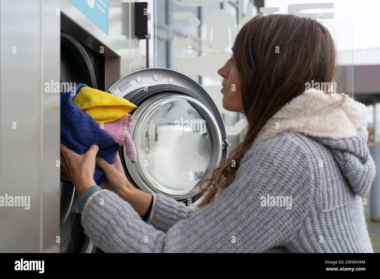 Frau, die eine Waschmaschine in einen Waschsalon stellt Stockfoto
