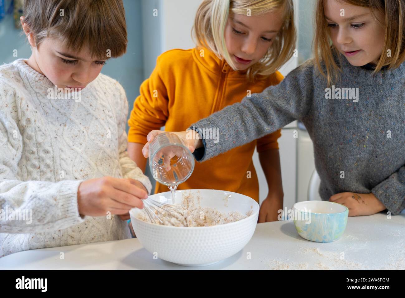 Drei Kinder bereiten gemeinsam einen selbstgemachten Pizzateig vor Stockfoto