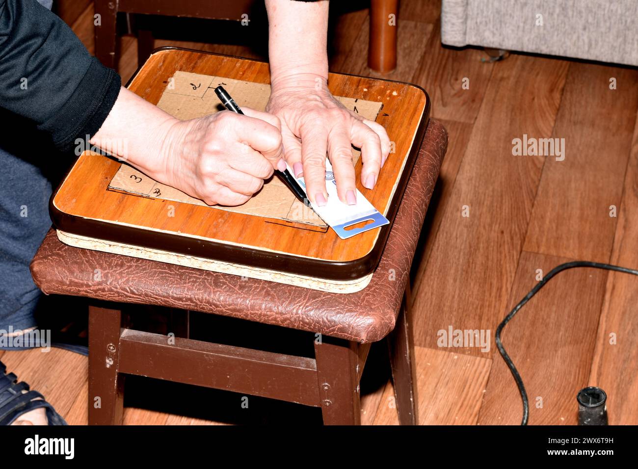 Möbelreparatur. Der Zimmermann macht Markierungen auf dem Brett des Stuhlsitzes für zukünftige Löcher. Stockfoto
