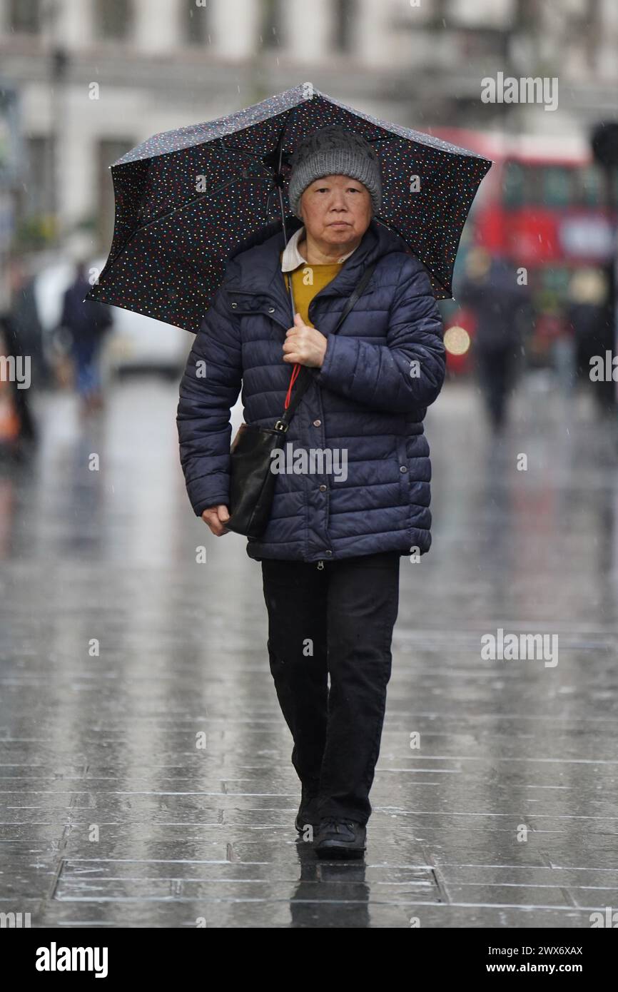 Eine Person nimmt Deckung unter einem Schirm, während sie durch den Regen am Leicester Square in London läuft. In Teilen Südwestenglands und Wales ist Schnee gefallen. Laut Wettervorhersage bewegt sich ein Gebiet mit Regen, Schneeregen und Bergschnee nach Norden durch Großbritannien, während sich Urlauber auf Osterausflüge vorbereiten. Bilddatum: Donnerstag, 28. März 2024. Stockfoto