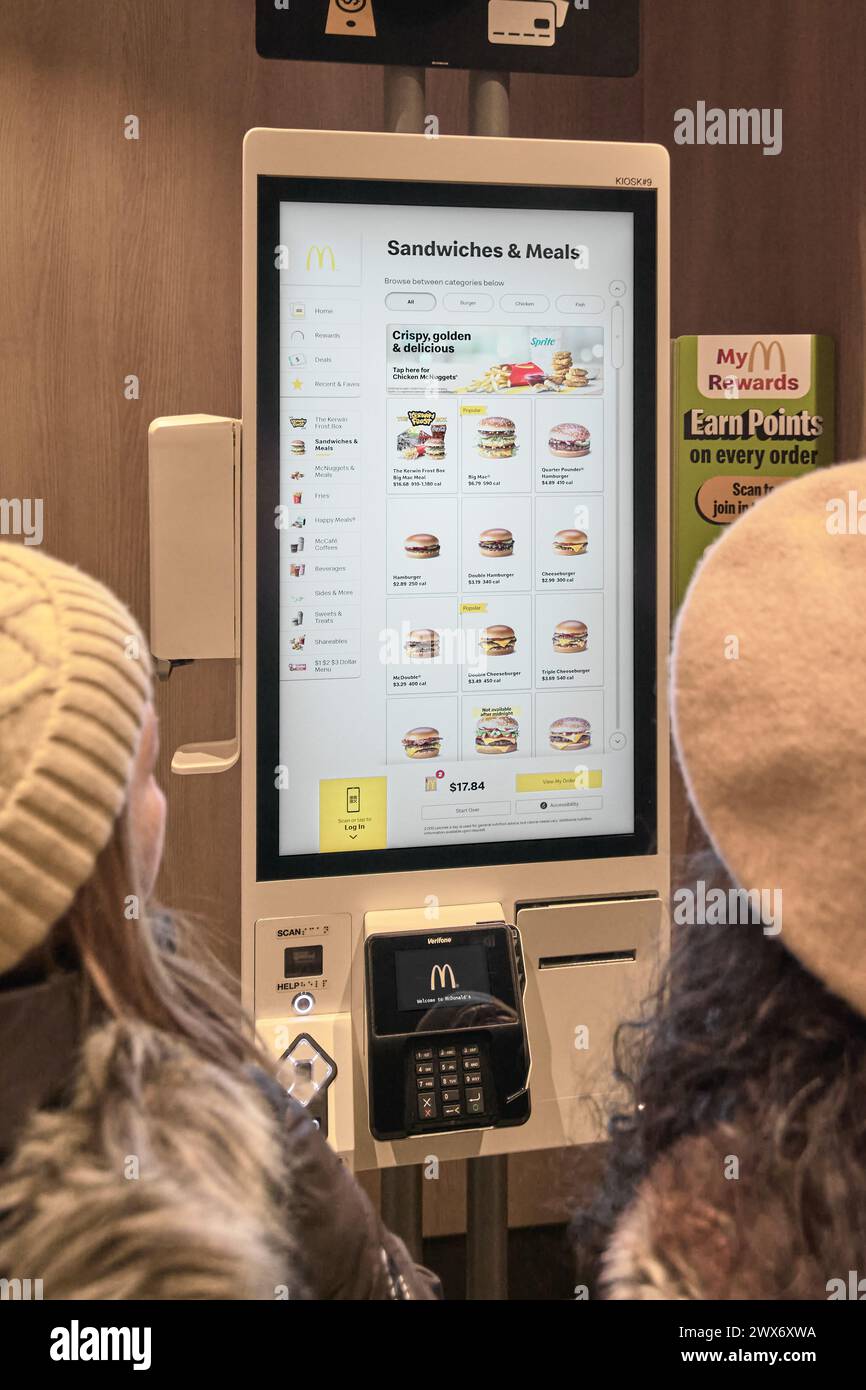 Nueva York, USA - 28. März 2024: Das Bild zeigt zwei Kunden, die einen Selbstbedienungskiosk bei einem McDonald's. Sie interagieren mit einem großen Touch sc Stockfoto
