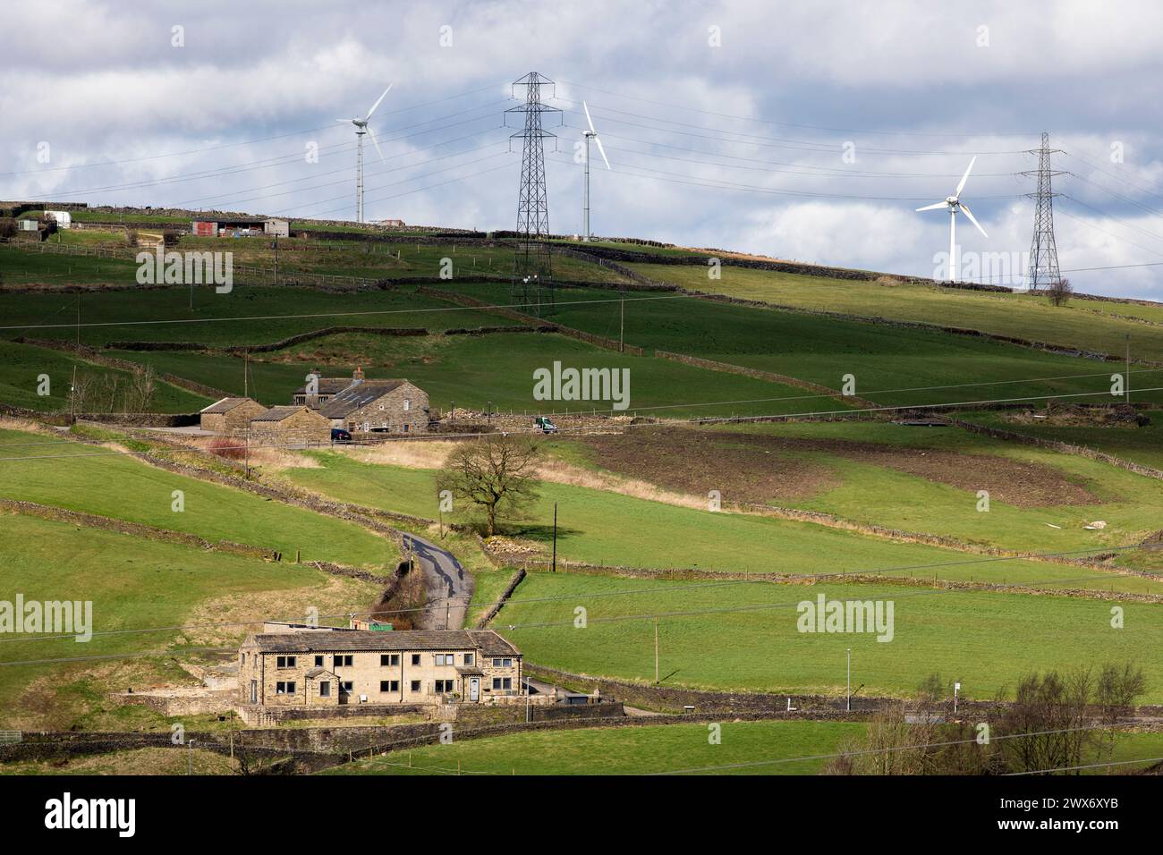 Windmühlen und Pylonen dominieren die Landschaft von Pennine und Moore über und um Farmen und Häuser in der Nähe von Queensbury und den Pennine Moors, die von den Bronte Schwestern berühmt wurden. Stockfoto