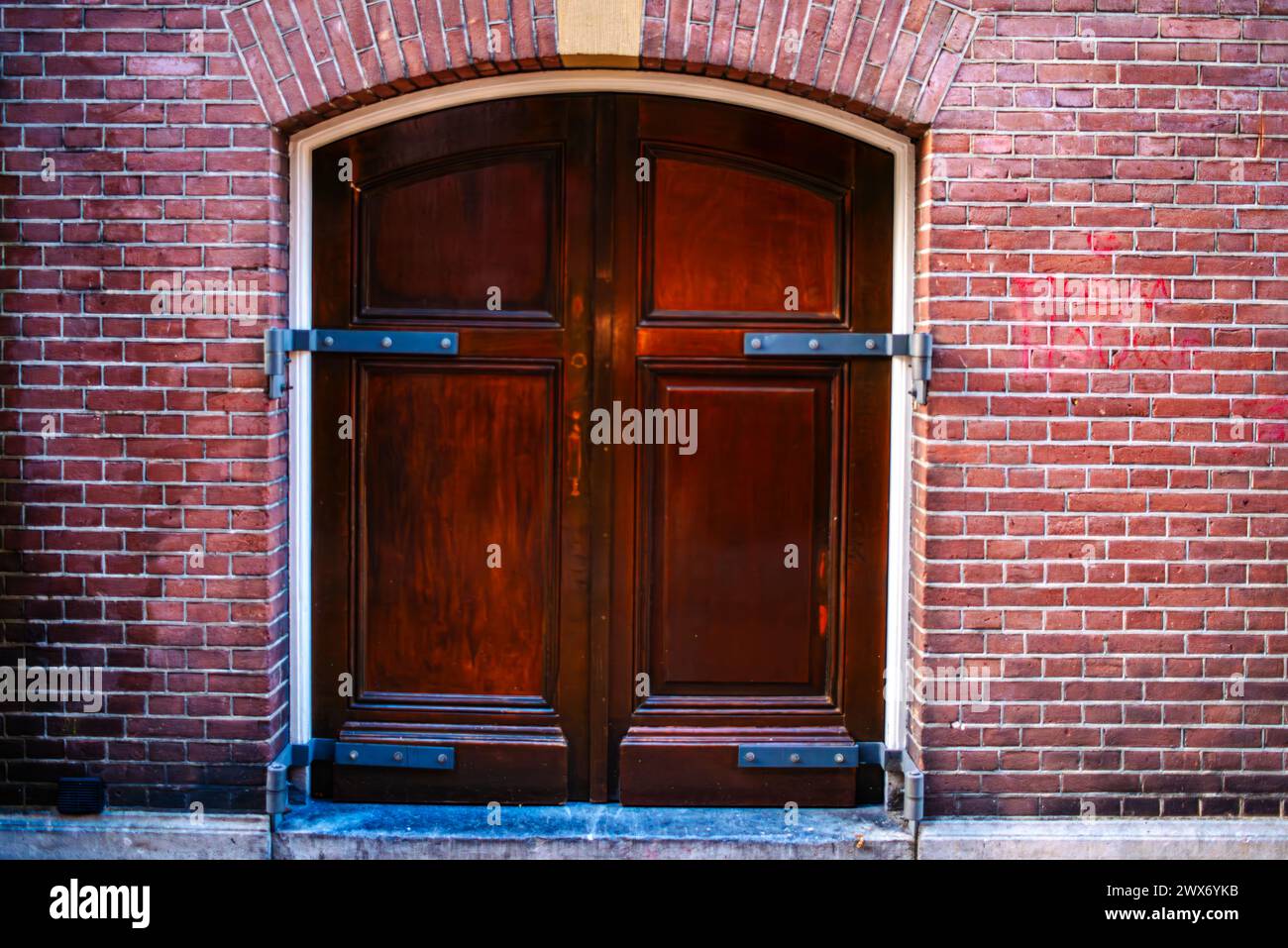 Eine Vintage-Tür ziert eine strukturierte Backsteinmauer in einer Amsterdamer Straße, die architektonischen Charme mit verwittertem urbanen Charme verbindet. Stockfoto