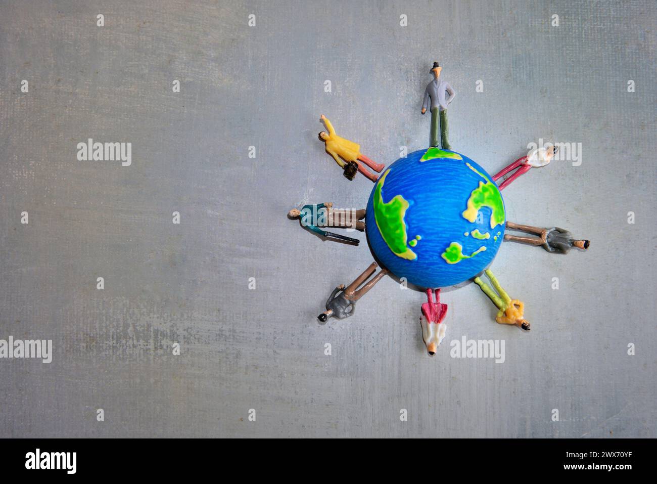 Eine Gruppe von Miniaturspielzeugen in verschiedenen Farben steht um einen Globus auf einer grauen Oberfläche. Kopierbereich für Text. Tag der Erde, Vielfalt und multirassische Vielfalt Stockfoto