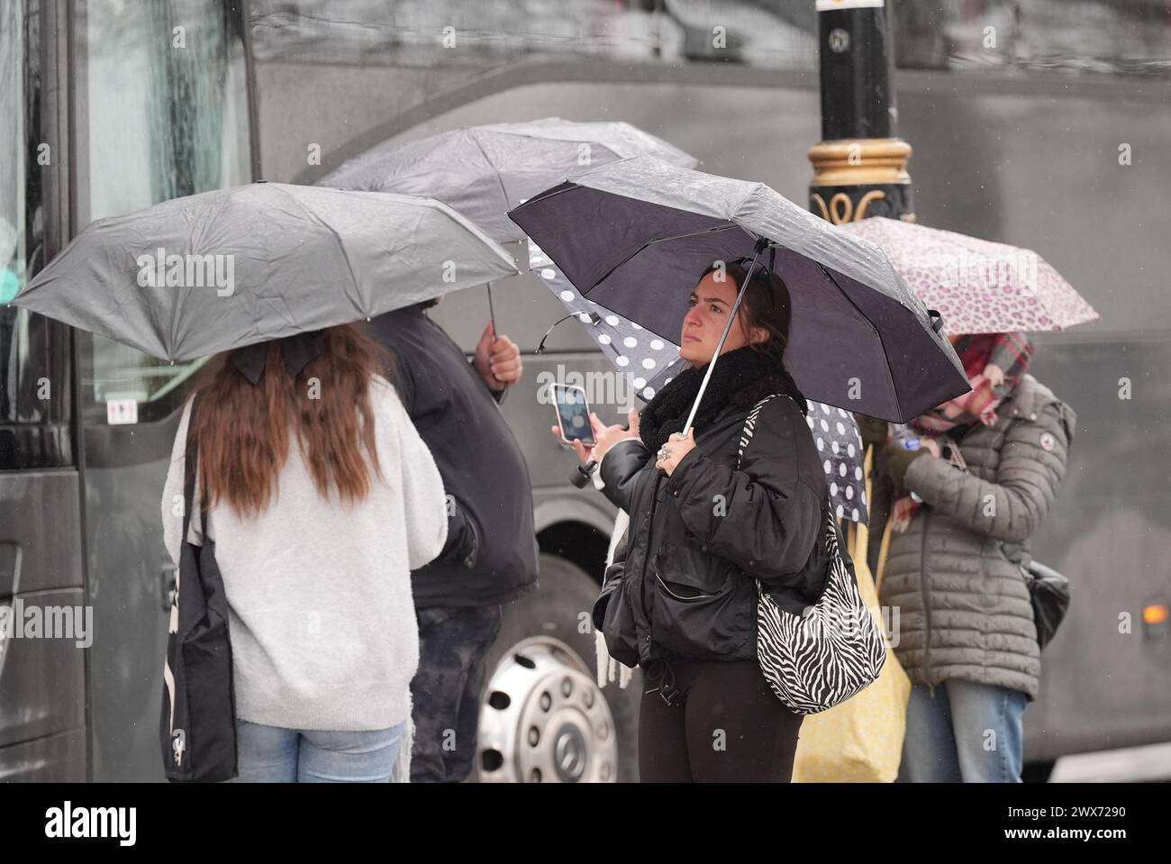 Die Menschen schützen vor dem Regen auf dem Embankment in London. Laut Wettervorhersage bewegt sich ein Gebiet mit Regen, Schneeregen und Bergschnee nach Norden durch Großbritannien, während sich Urlauber auf Osterausflüge vorbereiten. Bilddatum: Donnerstag, 28. März 2024. Stockfoto